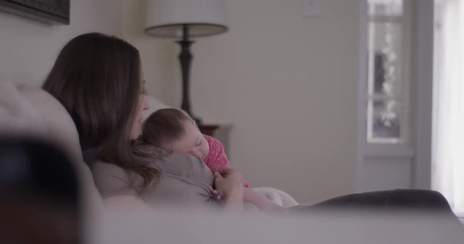 A woman snuggles with an infant on the couch