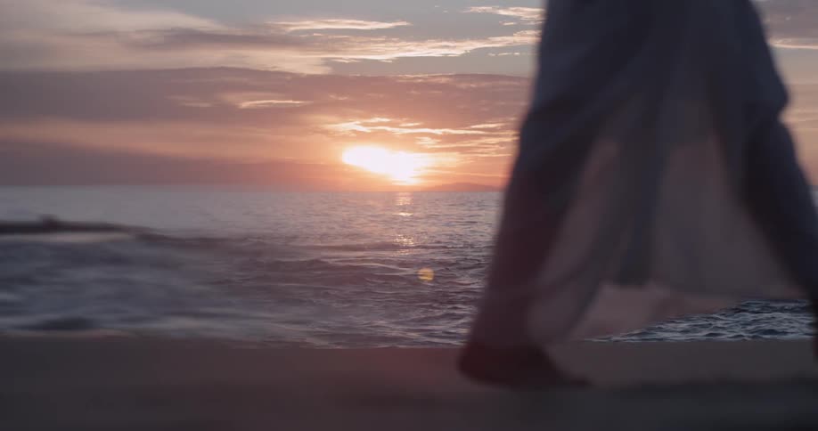 Woman walks along the beach as the sun sets over the ocean