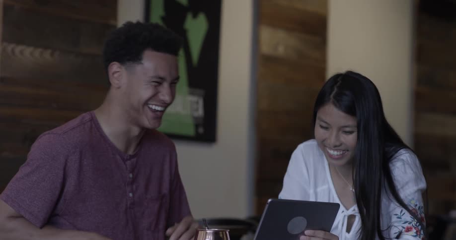 A man laughs at something a woman shows him on a tablet