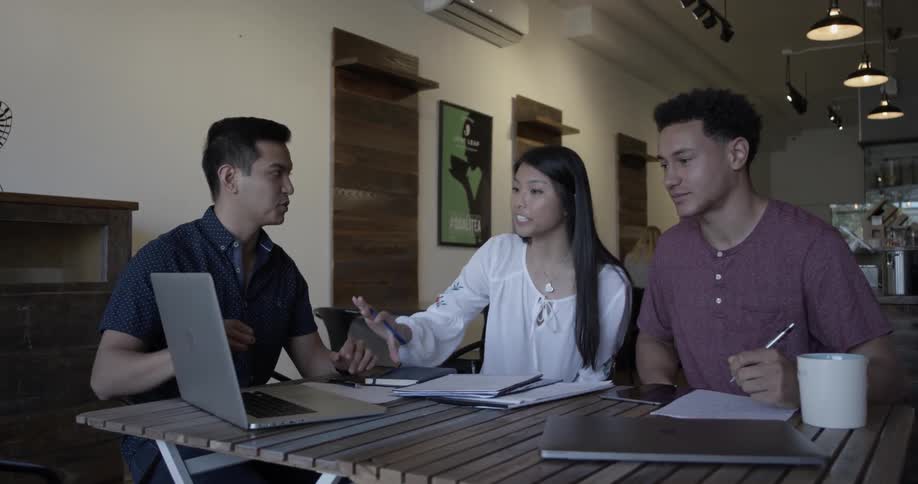 A man shows another man and a woman something on a laptop screen