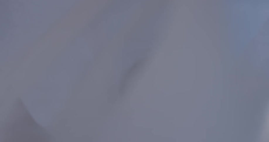 A woman holds a gauzy white scarf and waves it in the wind around her