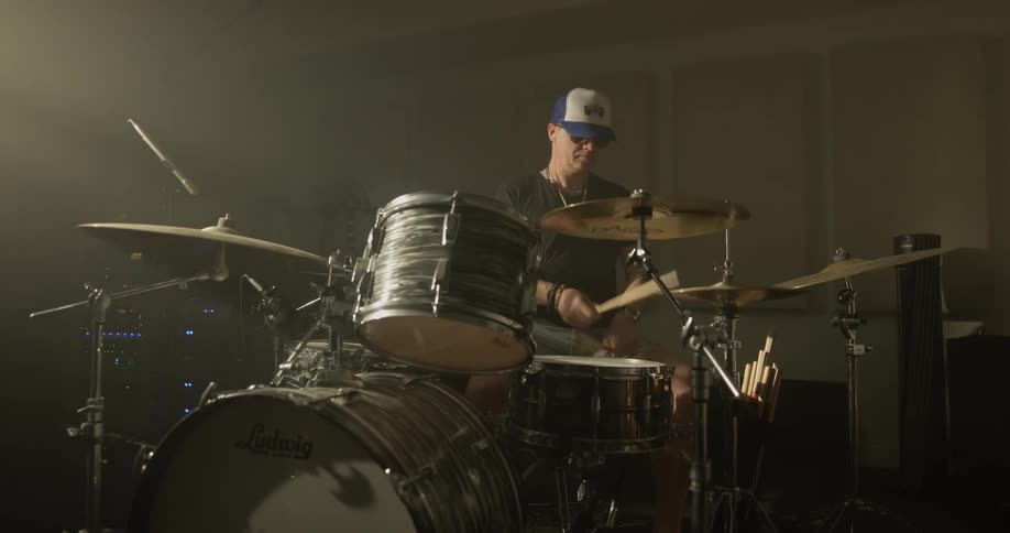Man plays drums in room with white light