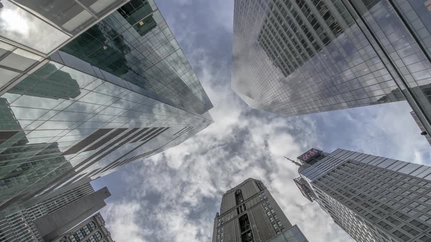 Reflections of clouds on shiny mirror like windows of buildings or skyscrapers as the camera looks up at the time lapse sky to see clouds rolling by