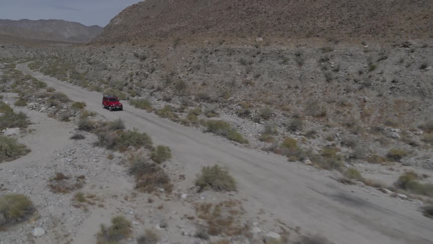 Red jeep drives down dirt road through desert