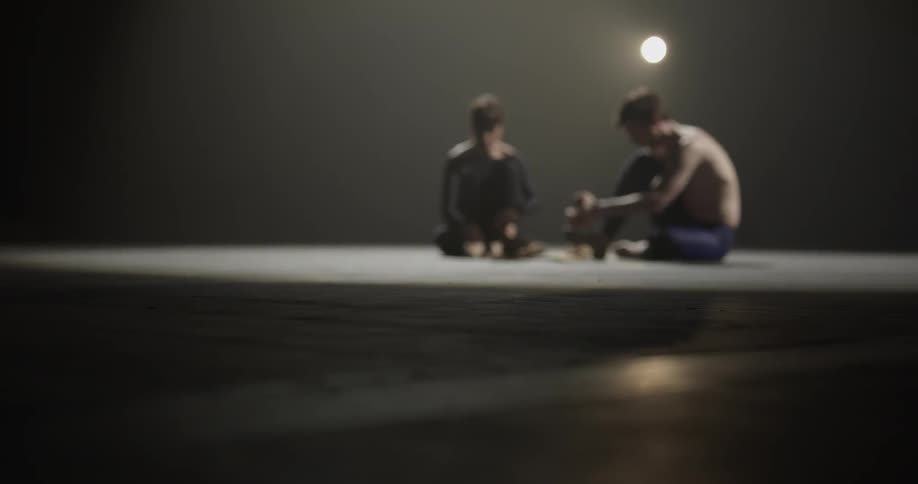 Two dancers sit white lacing up their footgear