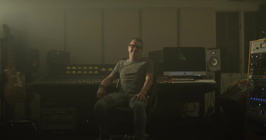 Man spins his chair away from audio mixer and smiles