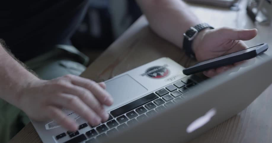 Man looks at phone while using laptop