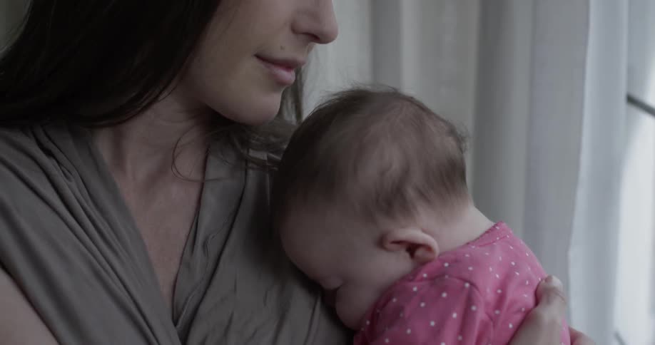 A woman holds a baby in front of a window