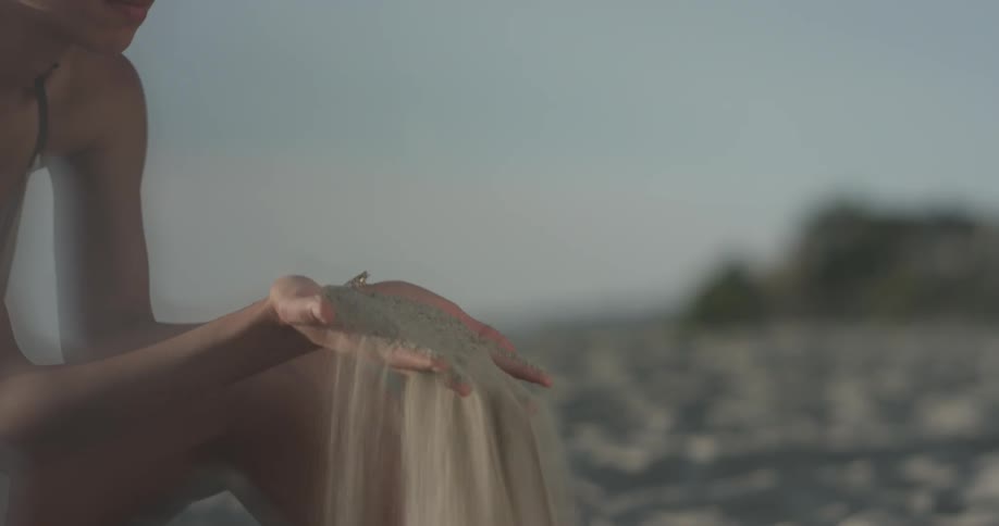 A woman picks sand up and drops it on the beach