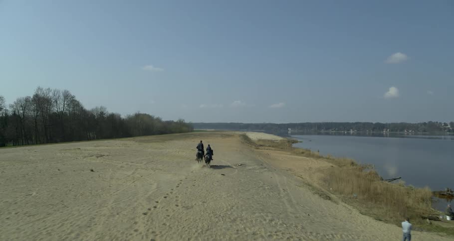 Two people ride horses next to a river