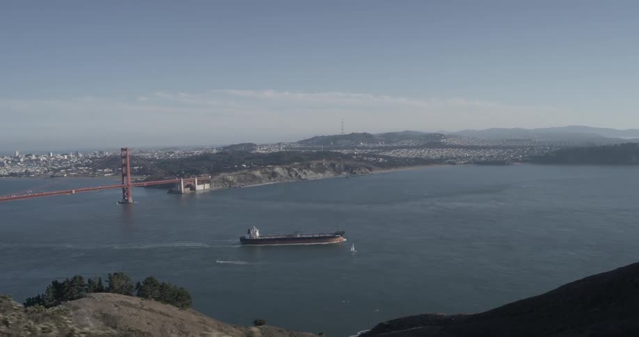 Hillside view of a barge sailing past a bridge