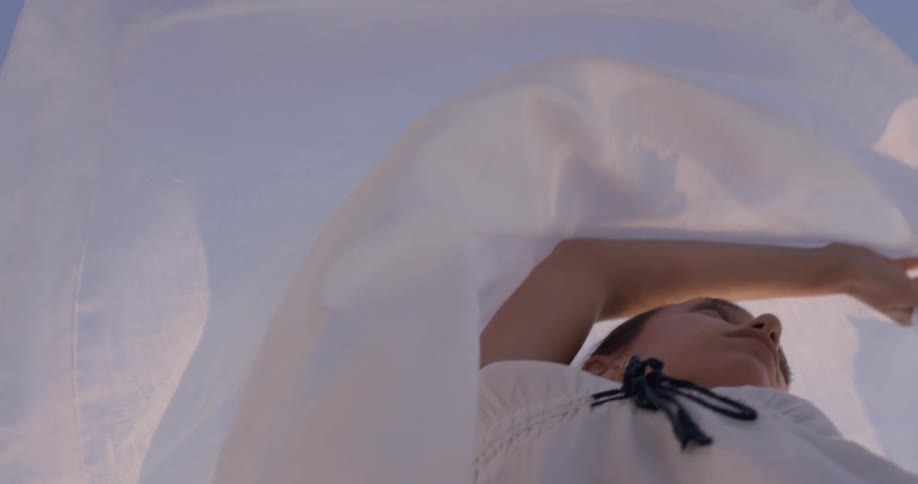 A woman twirls around in circles making a white sheet flutter in the wind