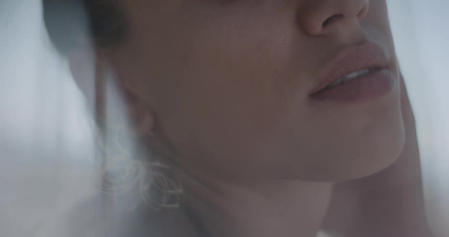 A woman blinks and looks at the camera then caresses her face and looks sensually on a sunlit dreamy day