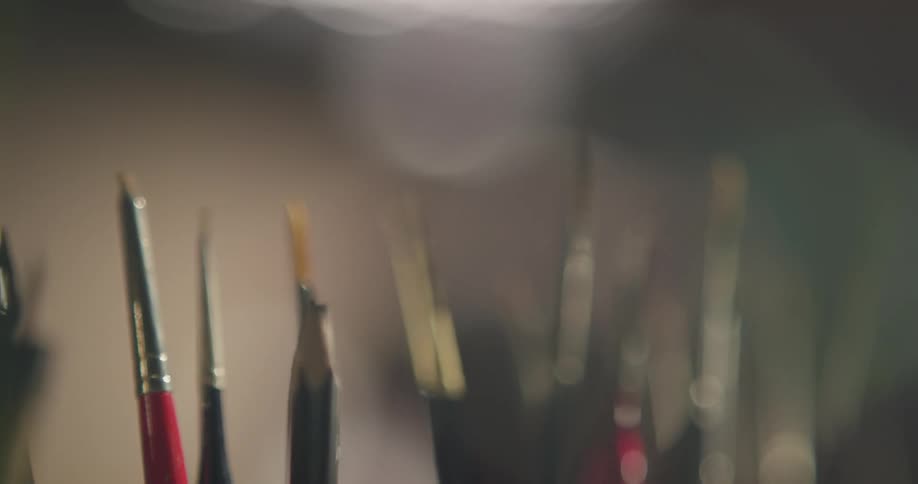 A lot of paint brushes that are sitting in jars