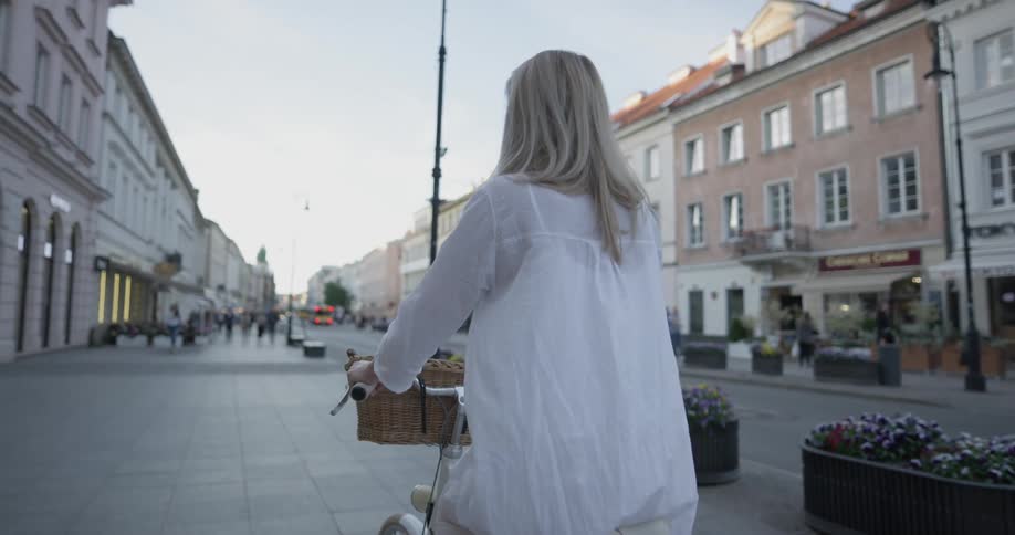 Woman rides bicycle down the street in front of shops