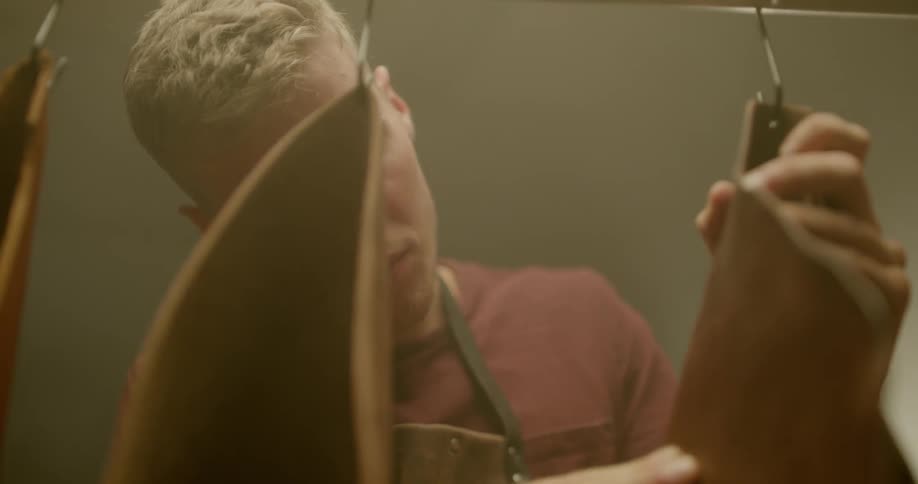 A man is looking over the leather pieces hanging