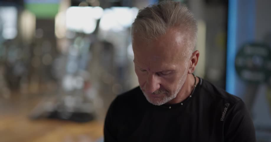 Grey haired man looking through his phone in a gym