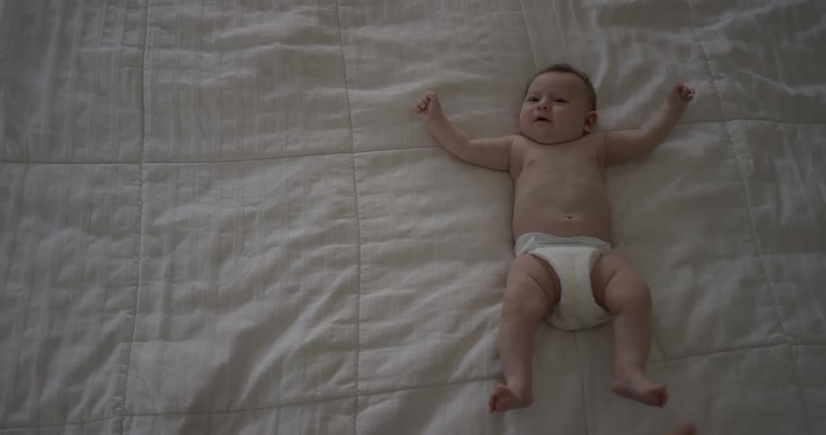 Baby lays on white bedspread and kicks feet
