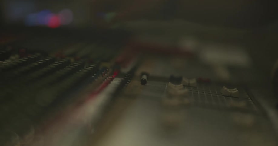 A man adjusts sliders and knobs on a music studio board