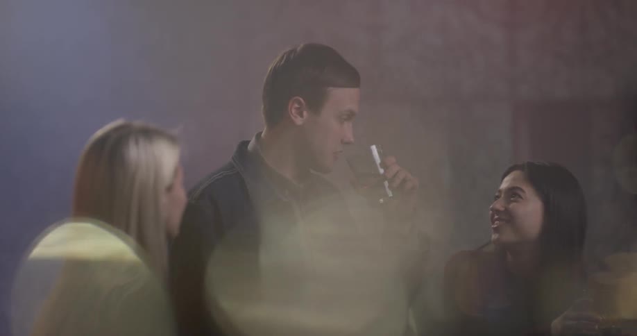 Two women sit and talk at a bar than a man comes up and starts talking to the two women