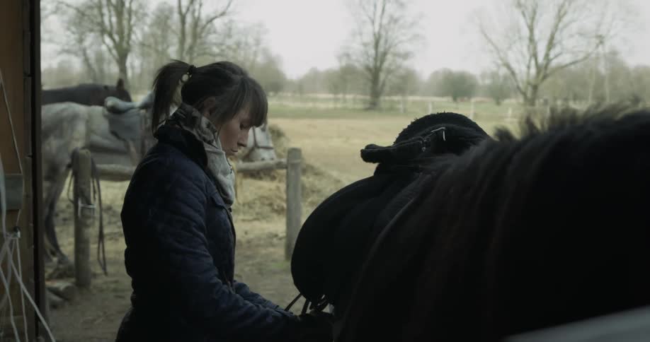 A woman places a saddle on a horse
