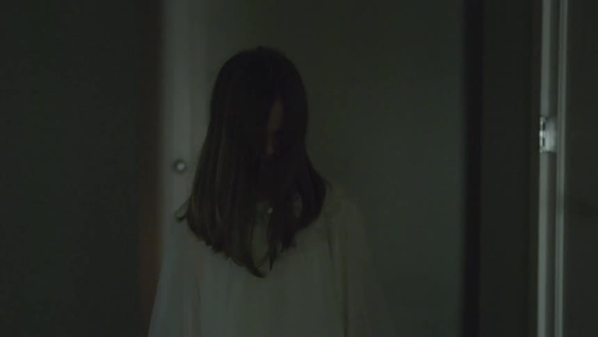 A girl carrying a doll down a hallway with hair over her face
