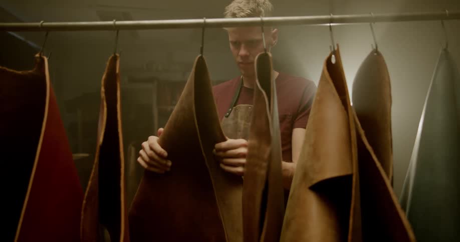 A man is feeling pieces of leather that are hanging up