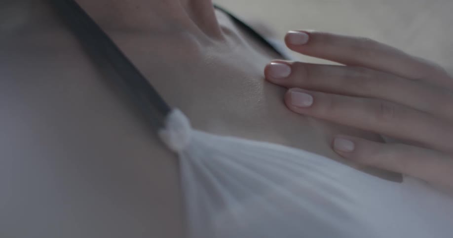 A woman runs her fingers along her face, throat, and chest