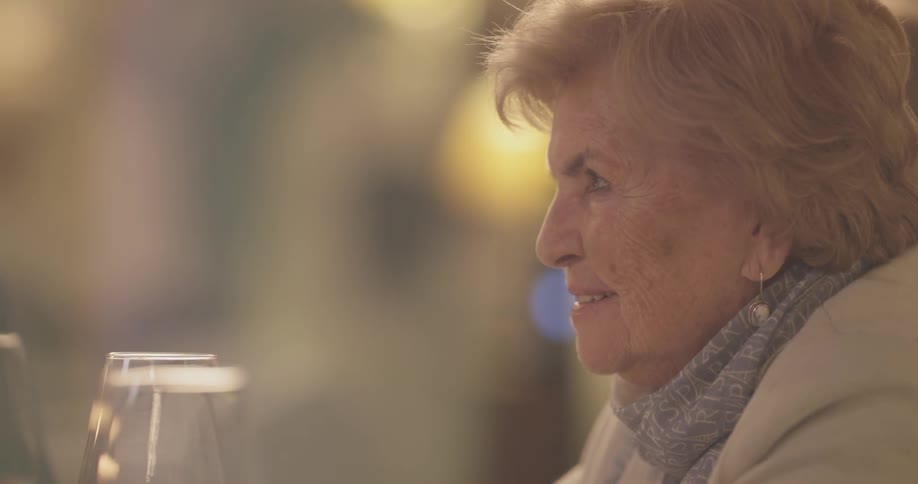 Elderly woman sits at a table with wine glasses