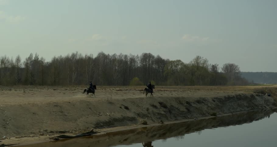 Two people riding horses next to a river