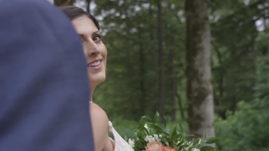 A bride and groom walk in a green forest