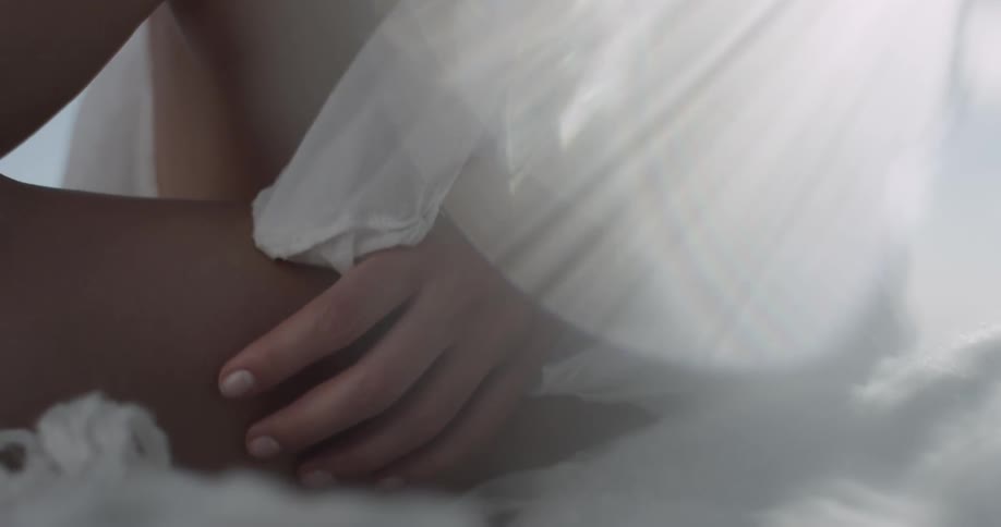 A woman is caressing her leg in slow motion with a thin white dress with sun beams and lens flares