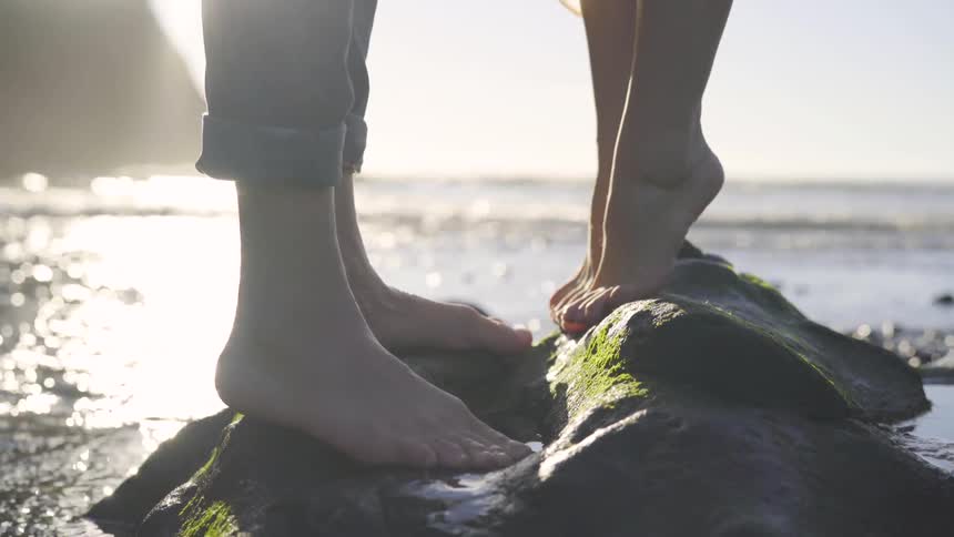 A child stands on tiptoe on a rock facing an adult standing on another rock