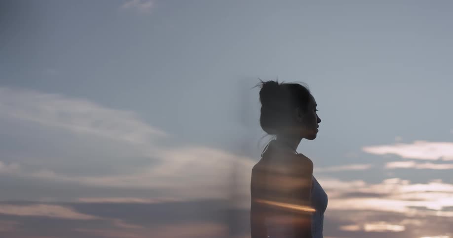 Sun sets while a woman looks in the distance