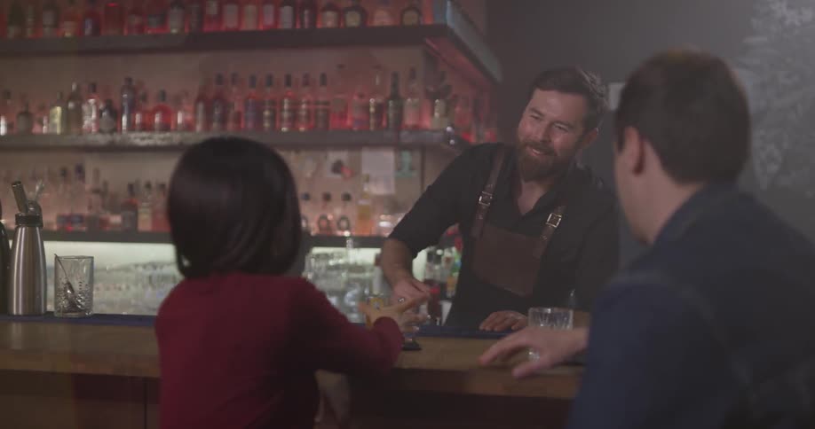 A man and woman sit talking at a bar and get drinks