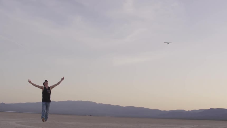 Man jumps around with his hands in the air and begins walking backwards as the plane flies by over head as the sun sets