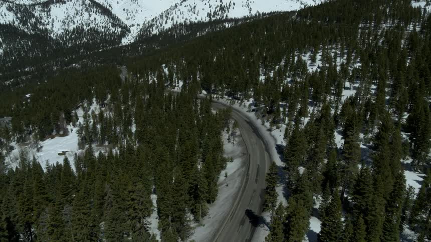 A car drives on a road through a snowy mountain pass
