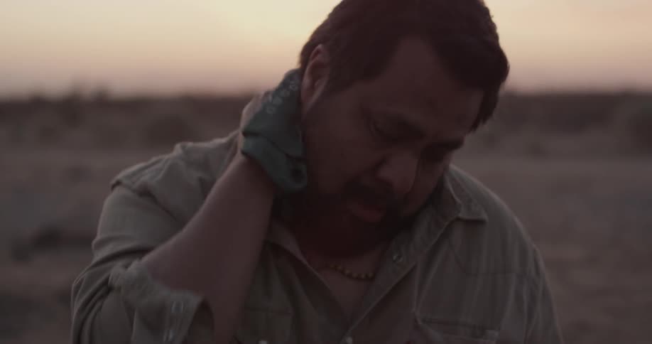 A man digging a hole in the desert at sunset