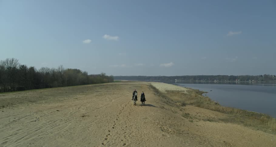 Two people ride horses near the water