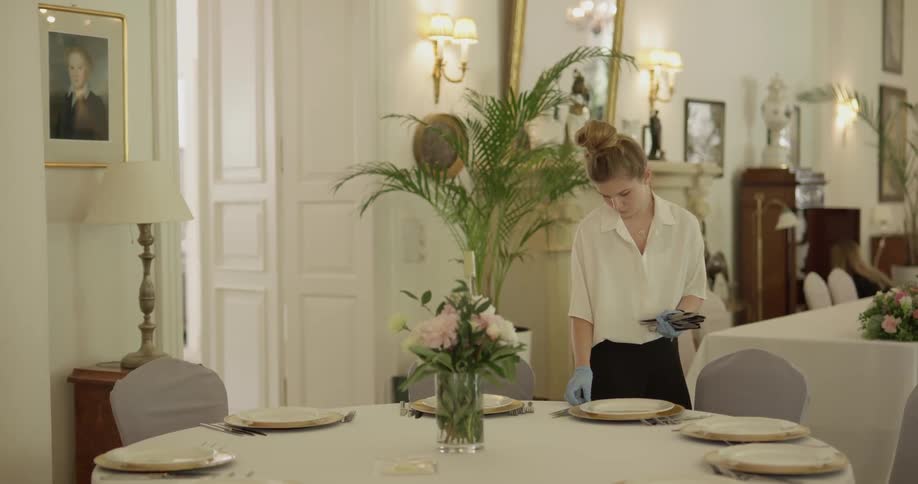 Woman is setting utensils on table inside dining hall