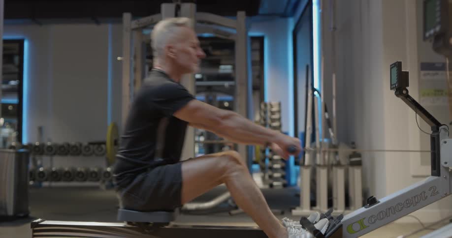 A fit man is exercising on a rowing machine in the gym