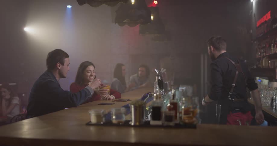A bartender is serving drinks to people sitting at a bar