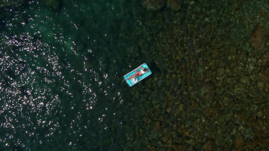 Woman on a raft in clear blue water with a rocky ground