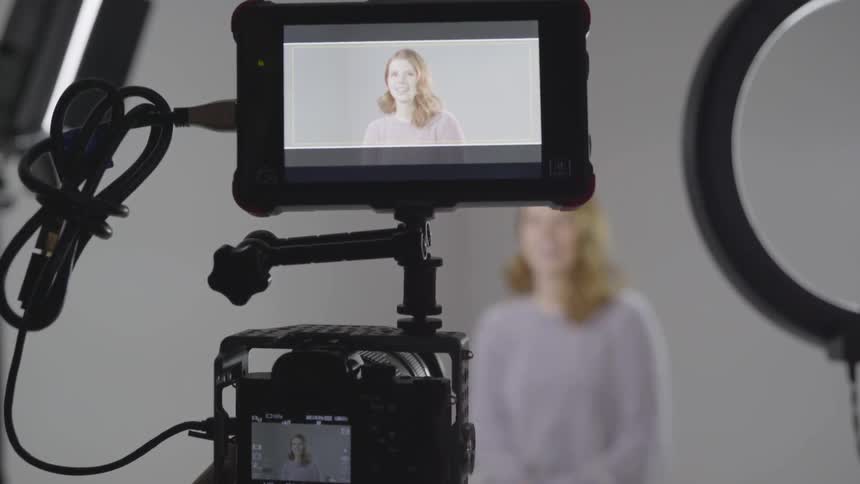 A woman stands in front of a camera professionally doing a scene with a white background