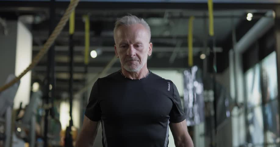 An elderly man curls dumbbells