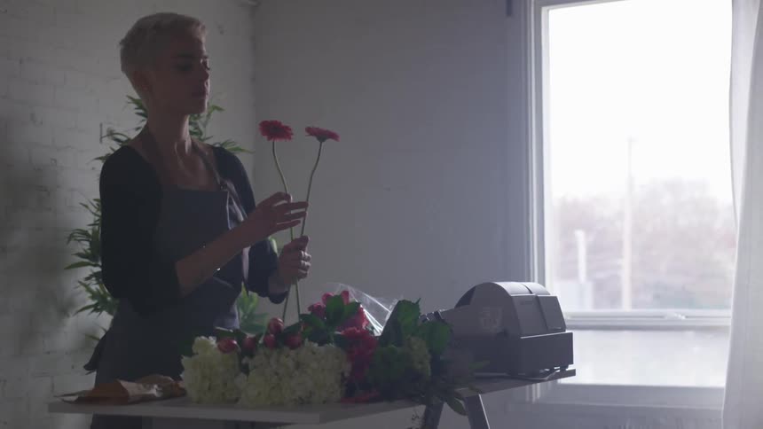 Woman stands at desk assorting flowers for an arrangement