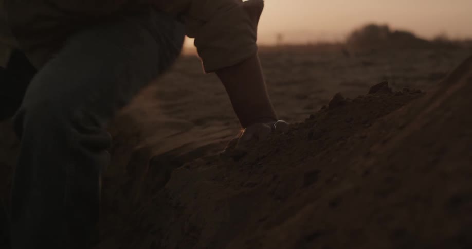 Person sitting down on a sandy ledge and standing up