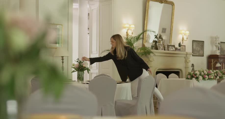 A woman walks to the table and places something in a vase