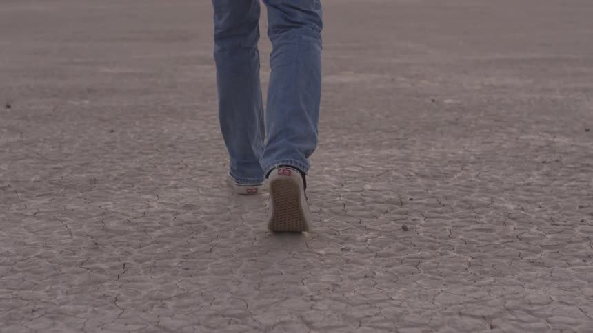 Man walks on dry barren desert on a bright sunny day
