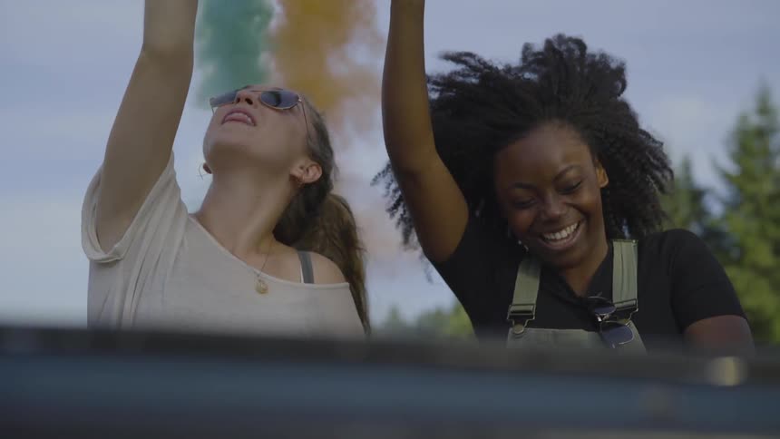 Two women hold up colored flares while riding in the back of a car